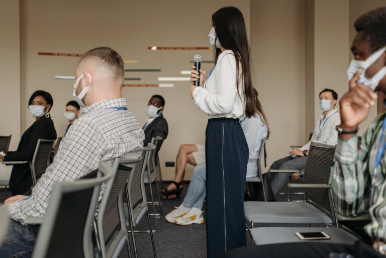 a woman holding a microphone standing in a room with a group of people